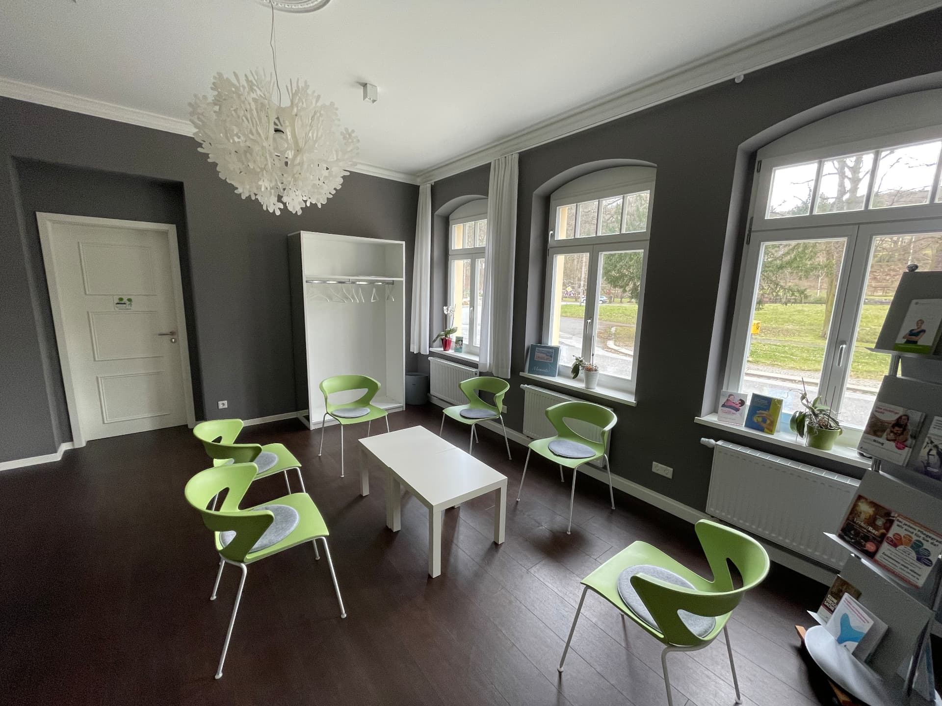 Wartezimmer mit hohen Fenstern und grünen Stühlen